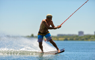A professional wakeboarder rides on the lake in sunny weather, performing figures