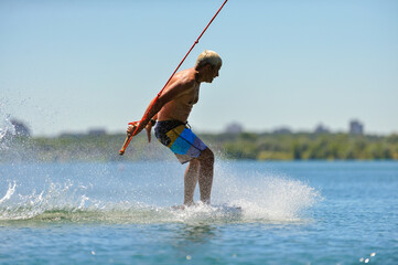 A professional wakeboarder rides on the lake in sunny weather, performing figures
