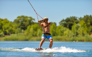 A professional wakeboarder rides on the lake in sunny weather, performing figures