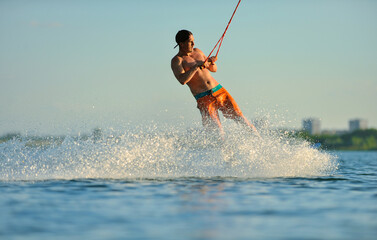 A professional wakeboarder rides on the lake in sunny weather, performing figures