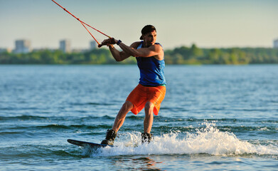 A professional wakeboarder rides on the lake in sunny weather, performing figures