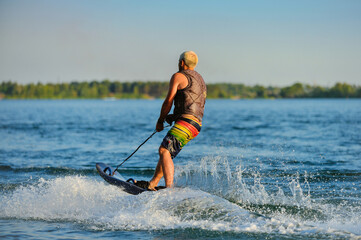 A professional wakeboarder rides on the lake in sunny weather, performing figures