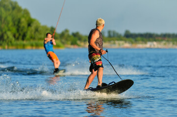 Professional wakeboarders ride on the lake in sunny weather with a good mood