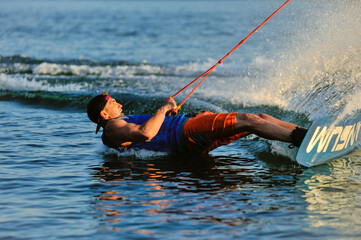 A professional wakeboarder rides on the lake in sunny weather, performing figures