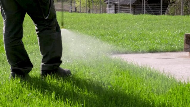 Farmer spraying pesticide on lawn field wearing protective clothing. Treatment of grass from weeds and dandelion. Pest control. Insecticide sprayer with a proper protection. Gardening care season.