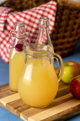 Jug and Bottle of Apple Juice with Pulp on Wooden Tray Blue Background Vertical © katekrsk