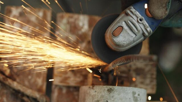 Man works with a circular saw. Construction worker cuts rebar with circular saw. Foreman in protective gloves using angle grinder and cutting metal tube. Glowing bright sparks flying.