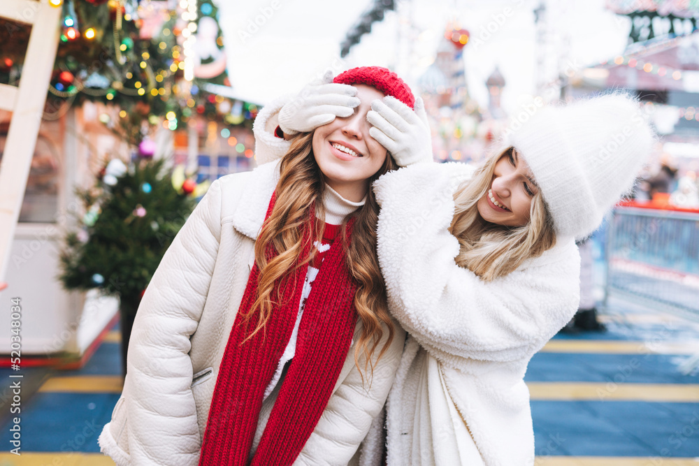 Wall mural Young happy women friends with curly hair in red having fun in winter street decorated with lights