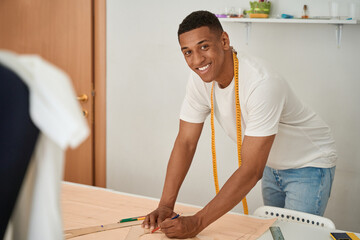 Happy male dressmaker making clothes drawings in atelier