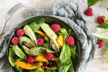 plate with salad with spinach, mango, avocado and raspberries on the table