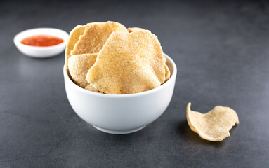 A bowl of shrimp crackers and sauce on a gray background, side view. Kerupuk udang - shrimp chips...