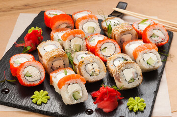 a large set of sushi rolls on a black stone plate
