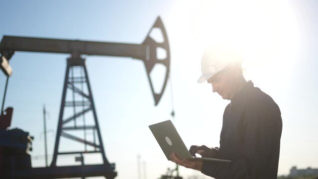 oil industry. engineer next to an oil rig. oil business production finance concept. gas production. a worker with a laptop sun monitors oil production next to an station. a worker in hard hat works