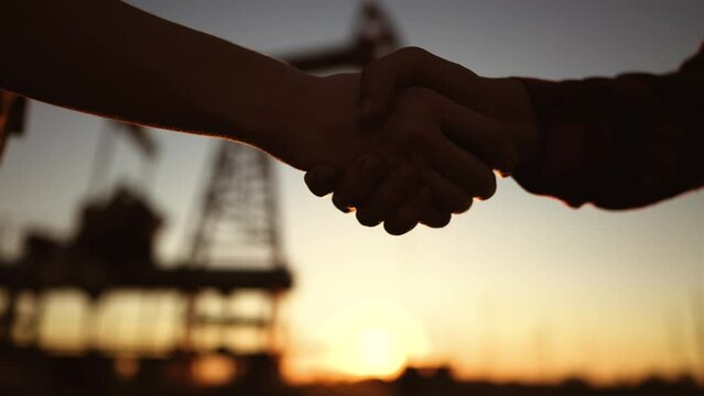 handshake oil contract. handshake a worker and businessman shaking hands against the backdrop of an oil pump. oil extraction business concept. silhouette handshake business close-up contract