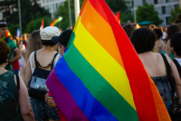 A brightly colored rainbow flag in the hand of an activist at the Pride month march. Lots of...