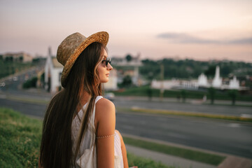 Portrait of a relaxed woman with hat looking forward at the horizon cityscape in the background copy space - 520354227