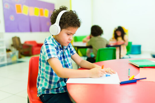 Autistic preschooler with headphones coloring alone in class