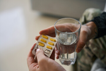 Glass of water and antidepressant medication in hands of soldier