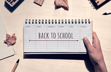 Back to school written on week planner in child, teenager hand. Low impact cardboard school...