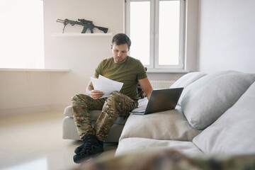Army man studying documents while clicking laptop at home