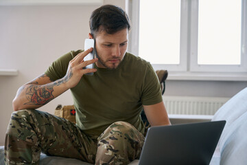 Soldier making a call while working online on laptop