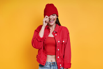 Playful young woman adjusting her hat and smiling against yellow background