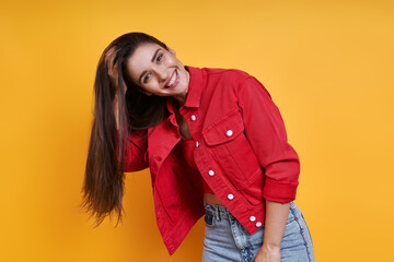 Attractive young woman adjusting her long hair against yellow background