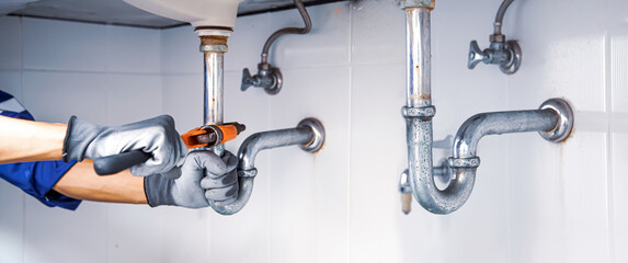 Technician plumber using a wrench to repair a water pipe under the sink. Concept of maintenance, fix water plumbing leaks, replace the kitchen sink drain, cleaning clogged pipes is dirty or rusty.