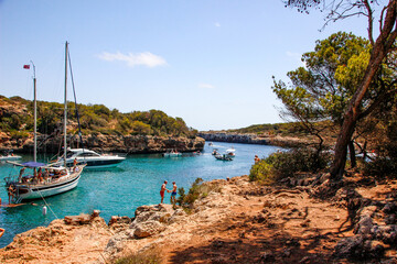 cove with boats, cliff with people, nature, forest and turquoise water, Mallorca, cala Sa nau, spain