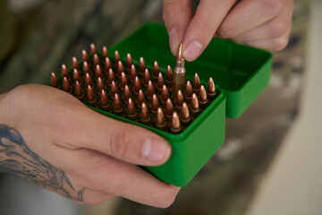 Army man picking up bullet from box of ammunition