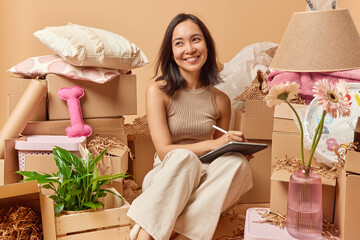 Happy Asian woman dressed in casual clothes uses tablet and stylus imagines design of her future...