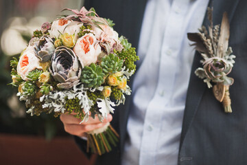 Bright wedding bouquet in hands of the groom