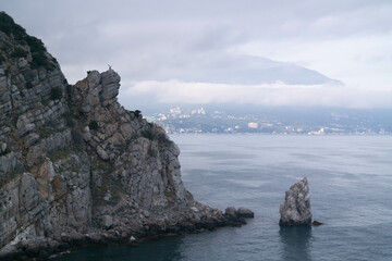 A rock in the sea with an eagle on top and a sail-shaped rock at the foot