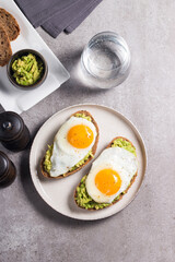 Avocado egg sandwich with a glass of water. Healthy light breakfast concept. Whole grain toasts with mashed avocado and fried eggs