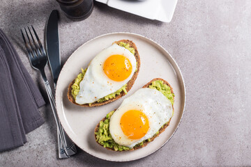 Avocado egg sandwich with a glass of water. Healthy light breakfast concept. Whole grain toasts with mashed avocado and fried eggs