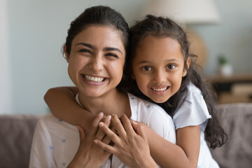 Happy beautiful young Indian mom and cute daughter kid home head shot. Cheerful mother piggybacking...
