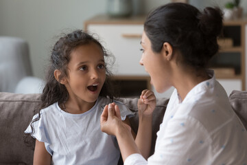 Indian female therapist training kid with hearing disability, deafness to use fingers for communication. Mom and cute daughter kid speaking sign language, talking, using hand gestures
