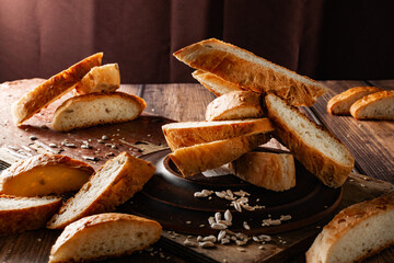 Homemade cakes, sliced ​​baguette, white bread with seeds and sesame seeds, golden crust, elements of wood and ceramics