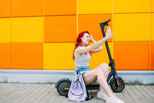 Woman uses a smartphone and an electric scooter in the summer in the city