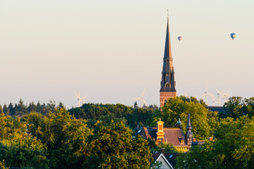 European cathedral tower surrounded by green trees at sunset with hot air balloons. Breda, the netherlands