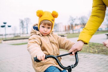 Obraz premium Grandmother teaches small child to ride bike for the first time in city spring