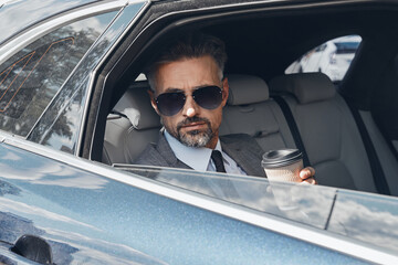 Mature businessman enjoying coffee and looking through a window while sitting in the car