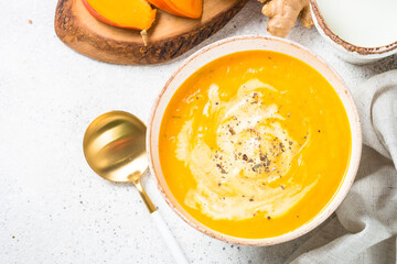 Pumpkin soup puree with cream and ginger in white bowl. Top view image at white stone table.