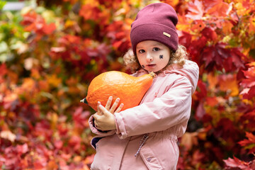 happy little cute girl with painting spider on cheek holding orange pumpkin for jack lantern....