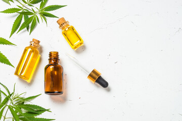 Cannabis oil in cosmetic bottles with dropper and fresh cannabis leaves at white background. Flat lay image with copy space.