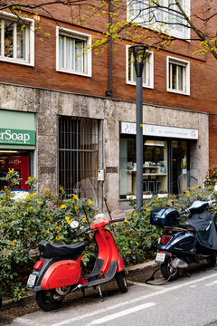 Bergamo, Italy - 21.04.21: Red and black motor scooters stand on the street against the background of a blooming flower bed