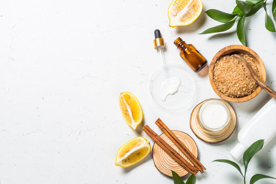 Homemade Cosmetic laboratory. Cosmetic bottles, cream, serum, sea salt, lemon and essential oils at white table. Flat lay image with copy space.