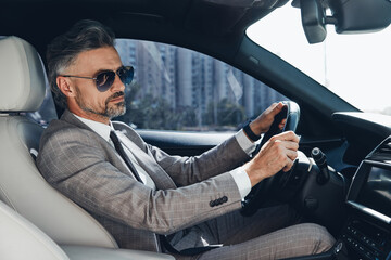 Confident mature man in formalwear and eyeglasses driving a car