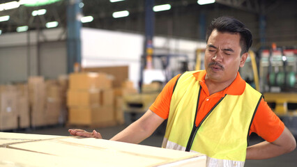 Asian man worker in a warehouse have an accident while carrying a heavy cardboard boxes with...