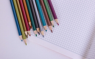 Fototapeta premium colored pencils and a notebook in a cage. school supplies. school. wooden pencils.